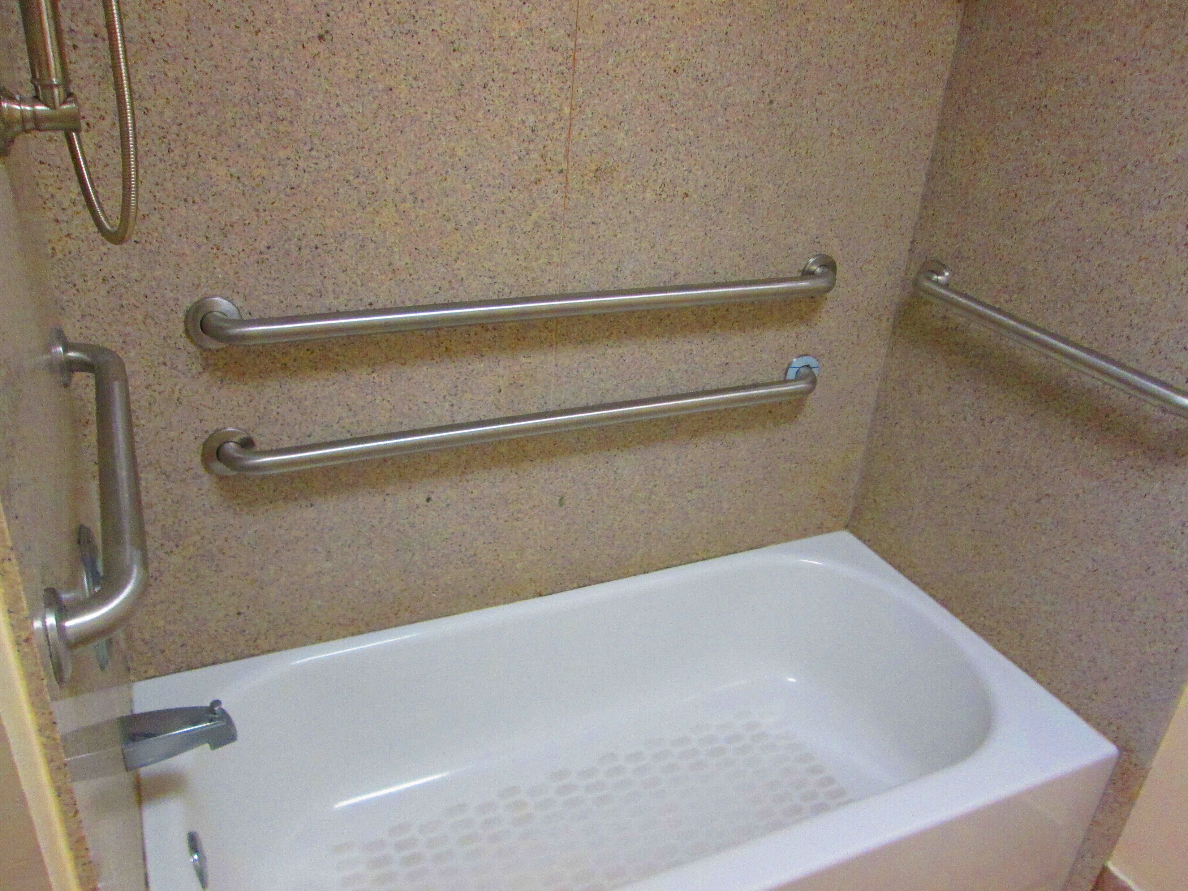 A bathroom with a white bathtub, grab bars, and a shower head.