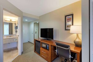 Habitación de hotel con escritorio de madera, televisor, lámpara, microondas y refrigerador pequeño.