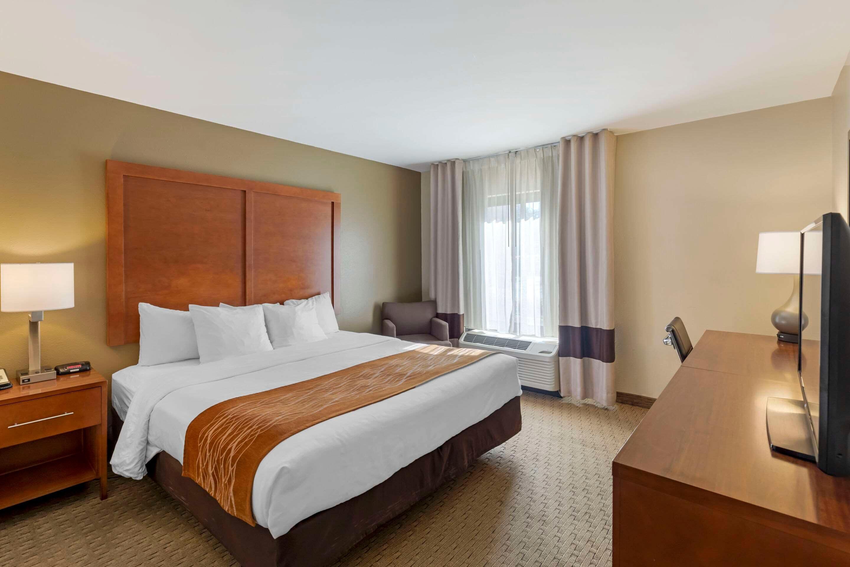 Ein Hotelzimmer mit einem großen Bett, einem Schreibtisch, einem Stuhl, einem Fernseher und einem Fenster mit Vorhängen.