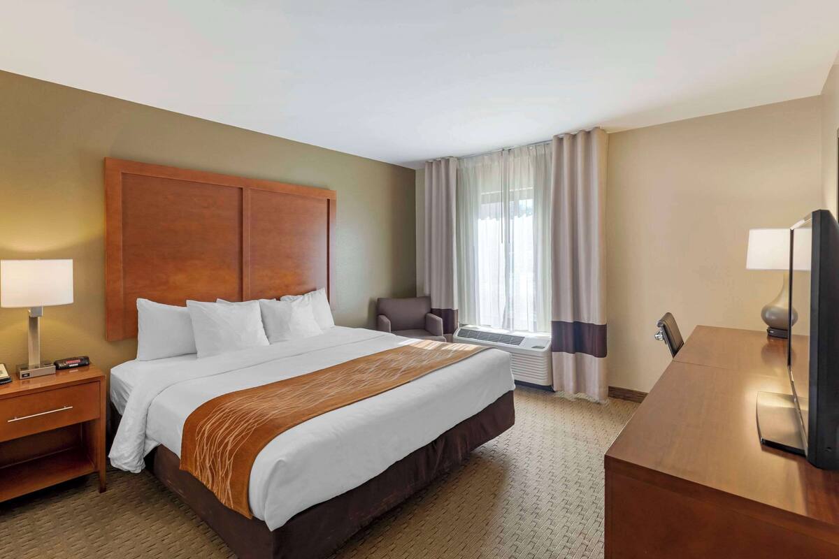 Habitación de hotel con una cama grande, un escritorio, una silla, un televisor y una ventana con cortinas.
