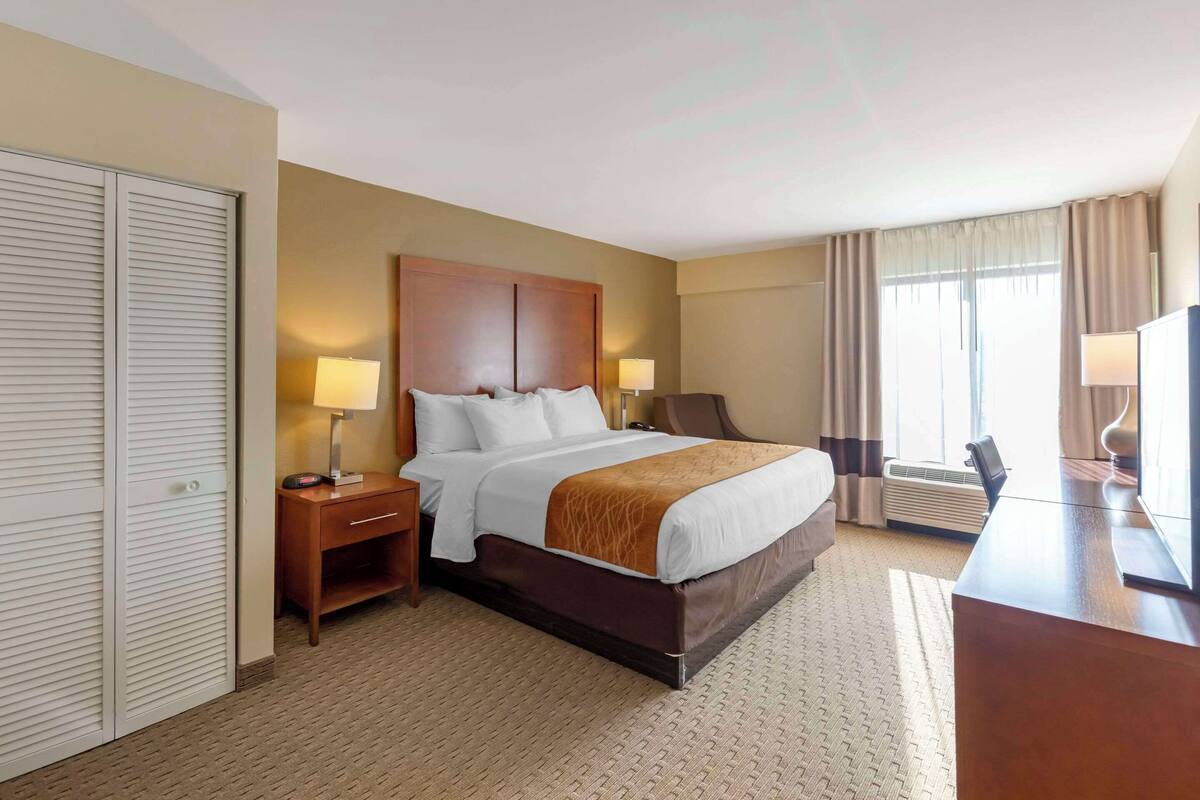 Una habitación de hotel con una cama grande, mesitas de noche con lámparas, un escritorio y una silla.