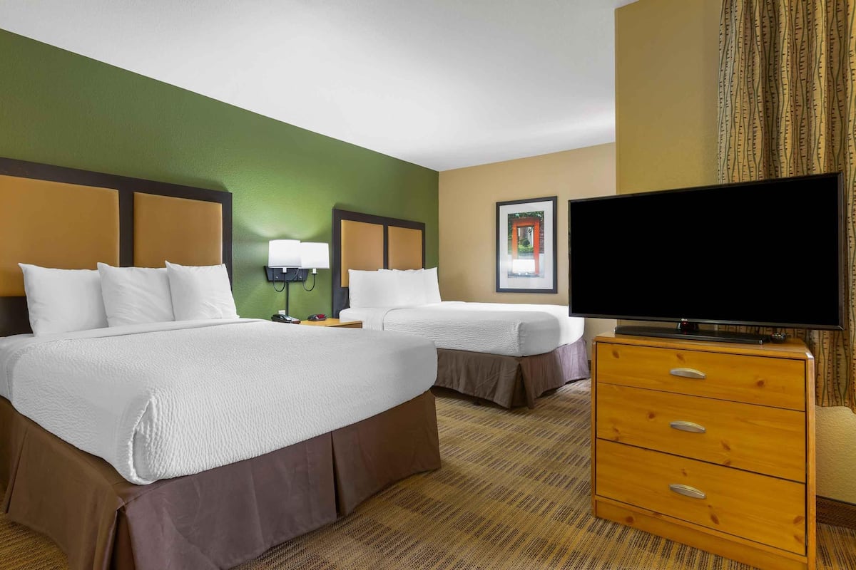 Une chambre d’hôtel avec deux lits, une télévision, une commode et un tableau encadré au mur.