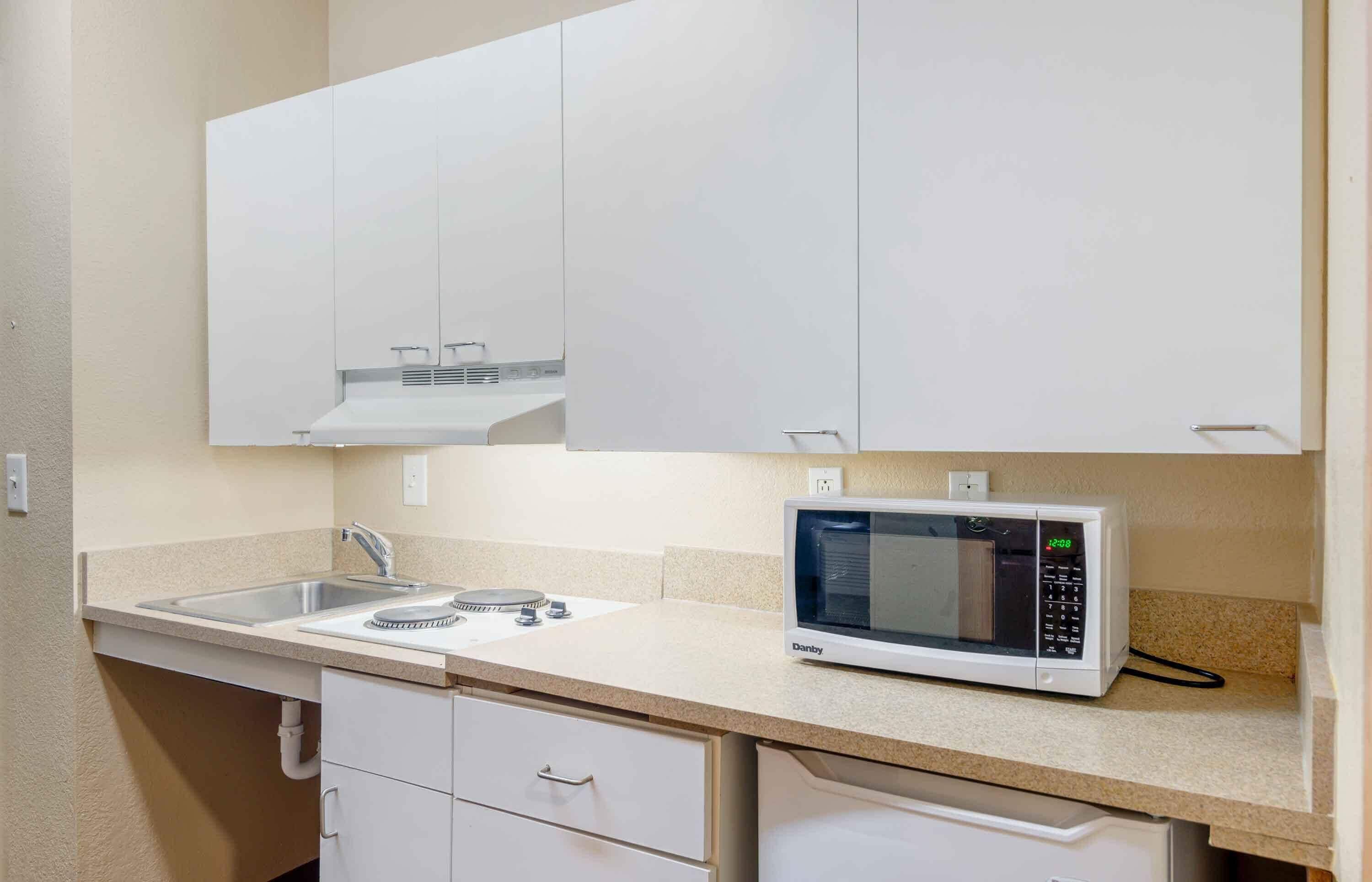 A kitchenette with a microwave, sink, and cabinets.