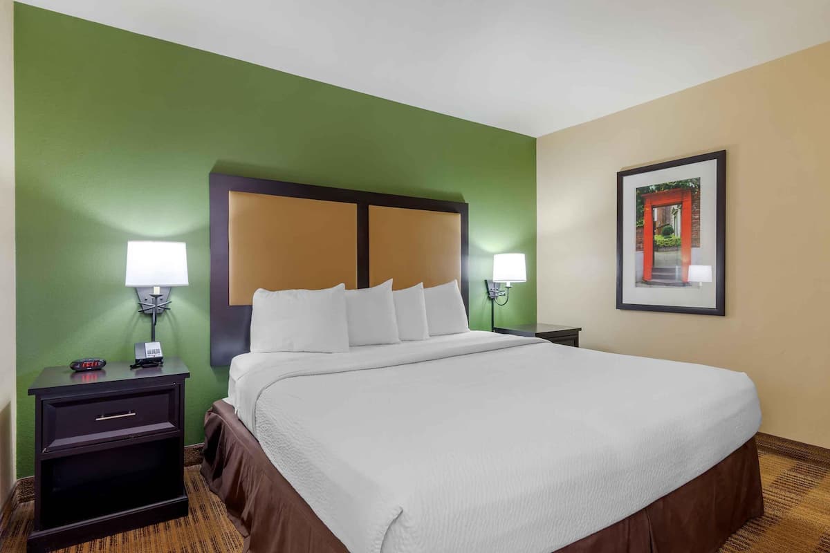 Une chambre d’hôtel avec un grand lit, deux tables de chevet avec des lampes, un tableau encadré au mur et un mur d’accent de couleur verte.