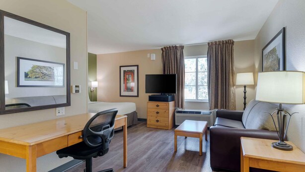 A hotel room with a bed, a desk, a chair, a television, a sofa, a lamp, and a window with curtains. - Extended Stay America Select Suites Atlanta Buckhead (Atlanta)