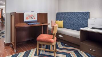 A hotel room with a wooden desk, a laptop, a chair, a sofa, and a printer.