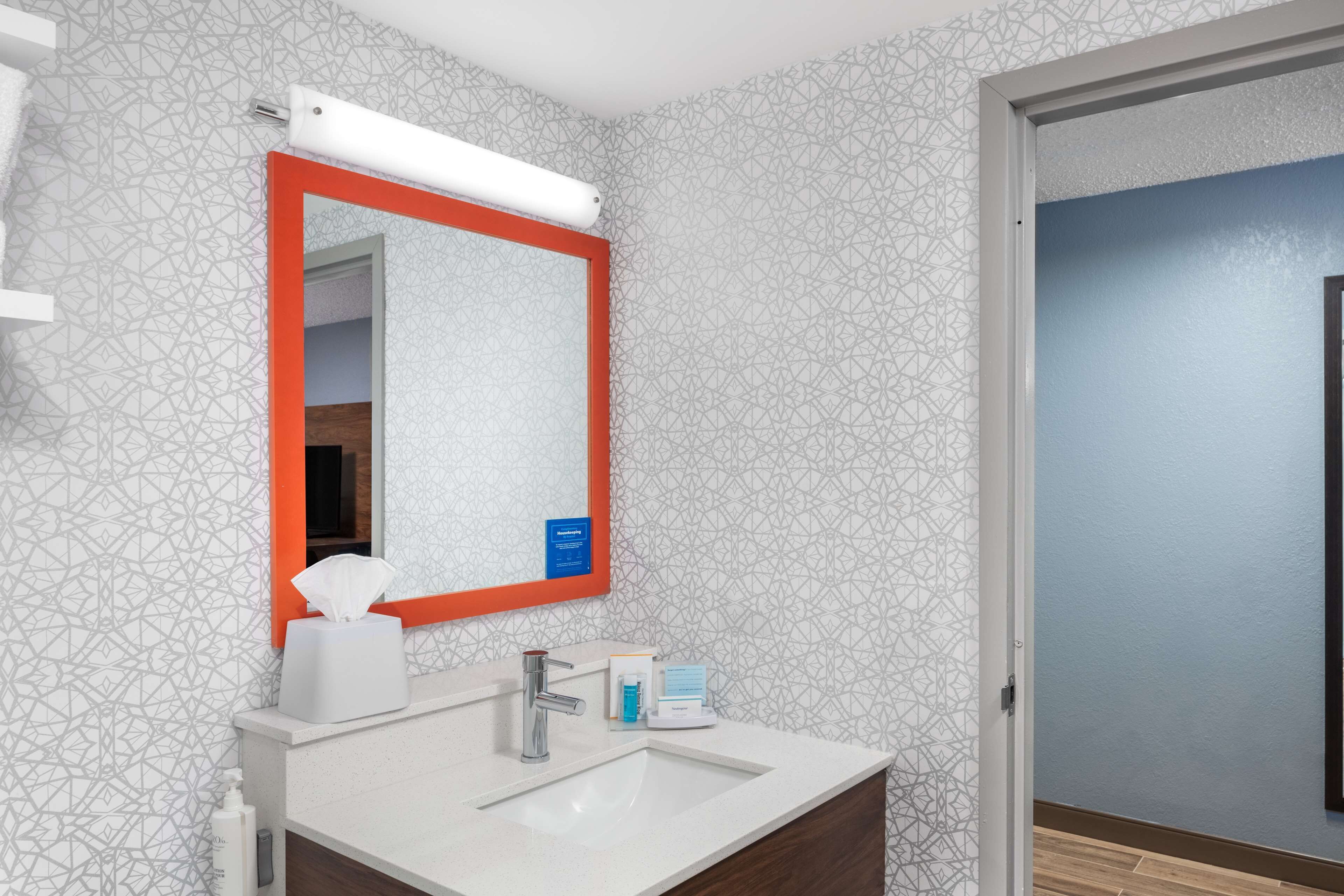 A bathroom with a white sink, a mirror with an orange frame, and patterned wallpaper.