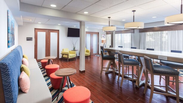 A hotel lobby with a long reception desk, multiple seating areas including a sofa and chairs, and a large window with curtains. - Hampton Inn Joliet-Plainfield I-55 (Joliet)