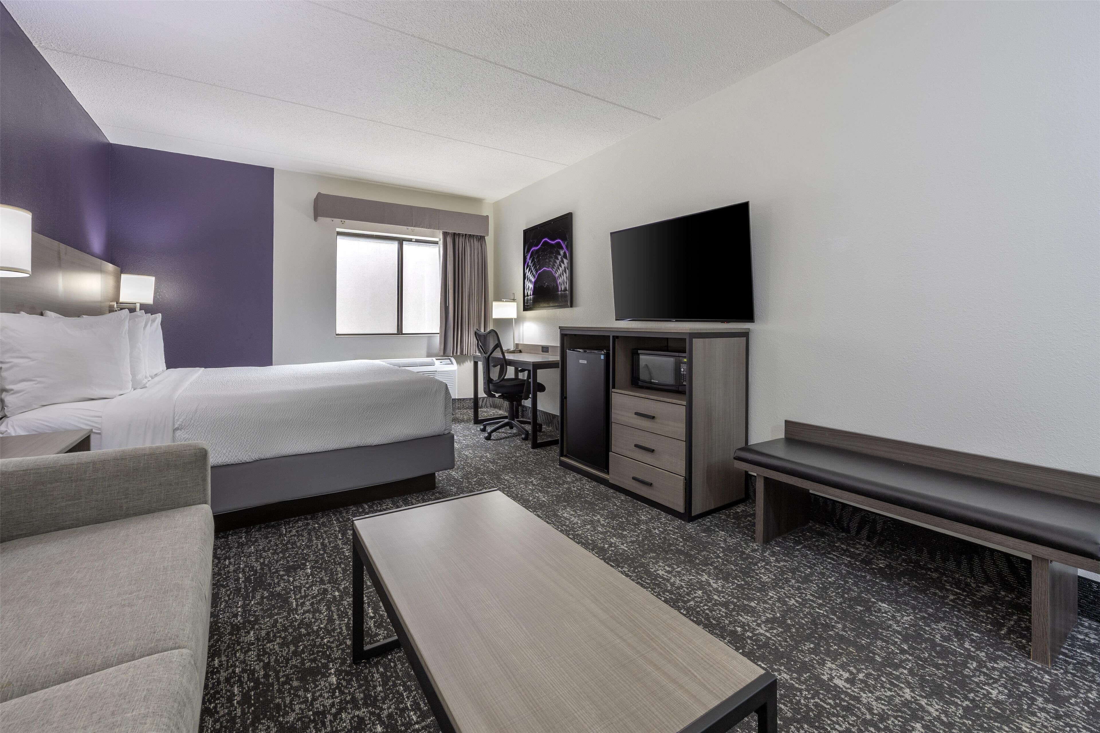 Habitación de hotel con cama, escritorio, silla, televisor y un banco.