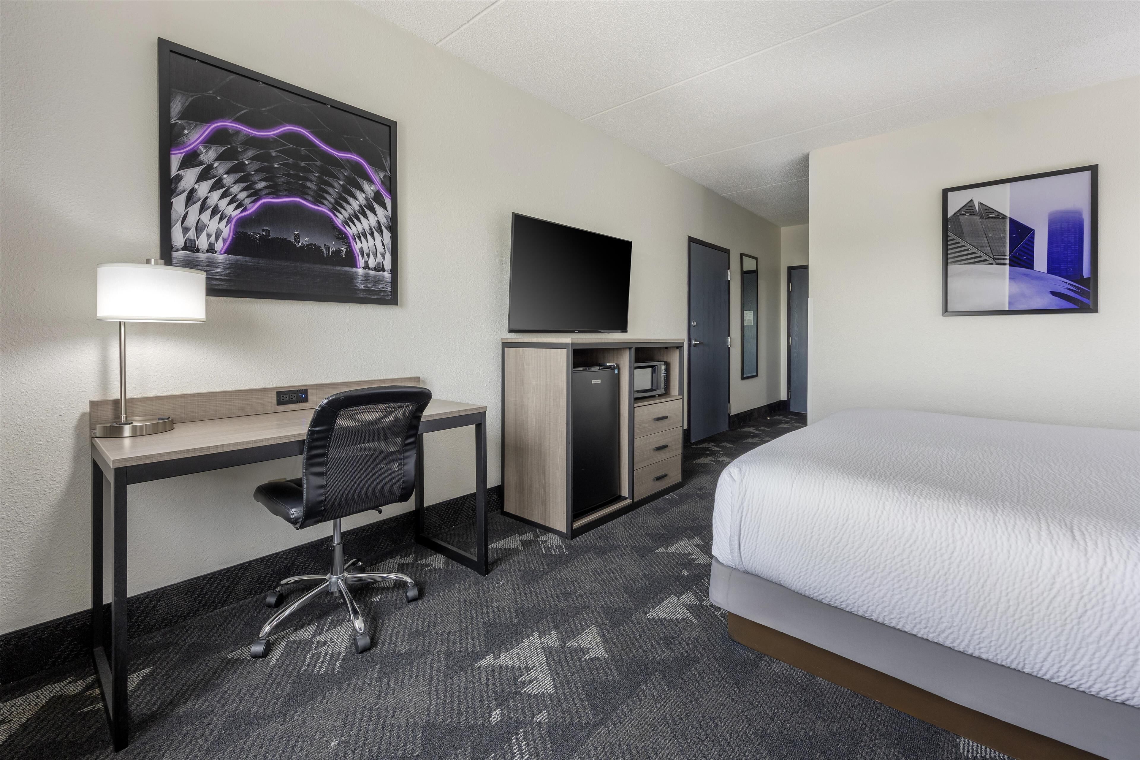 Habitación de hotel con cama, escritorio, silla, televisor y obras de arte en las paredes.