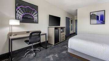 Habitación de hotel con cama, escritorio, silla, televisor y obras de arte en las paredes.