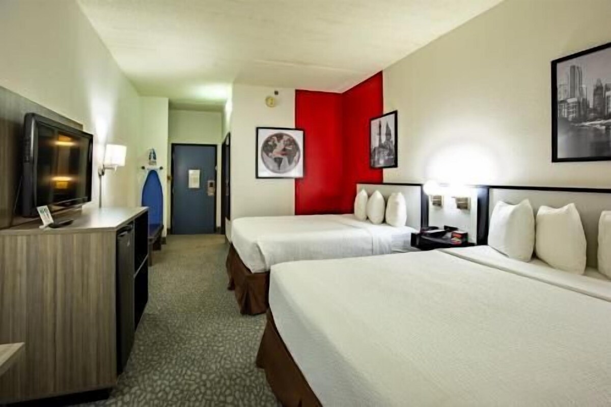 A hotel room with two beds, a desk with a computer, a television, and a red accent wall.