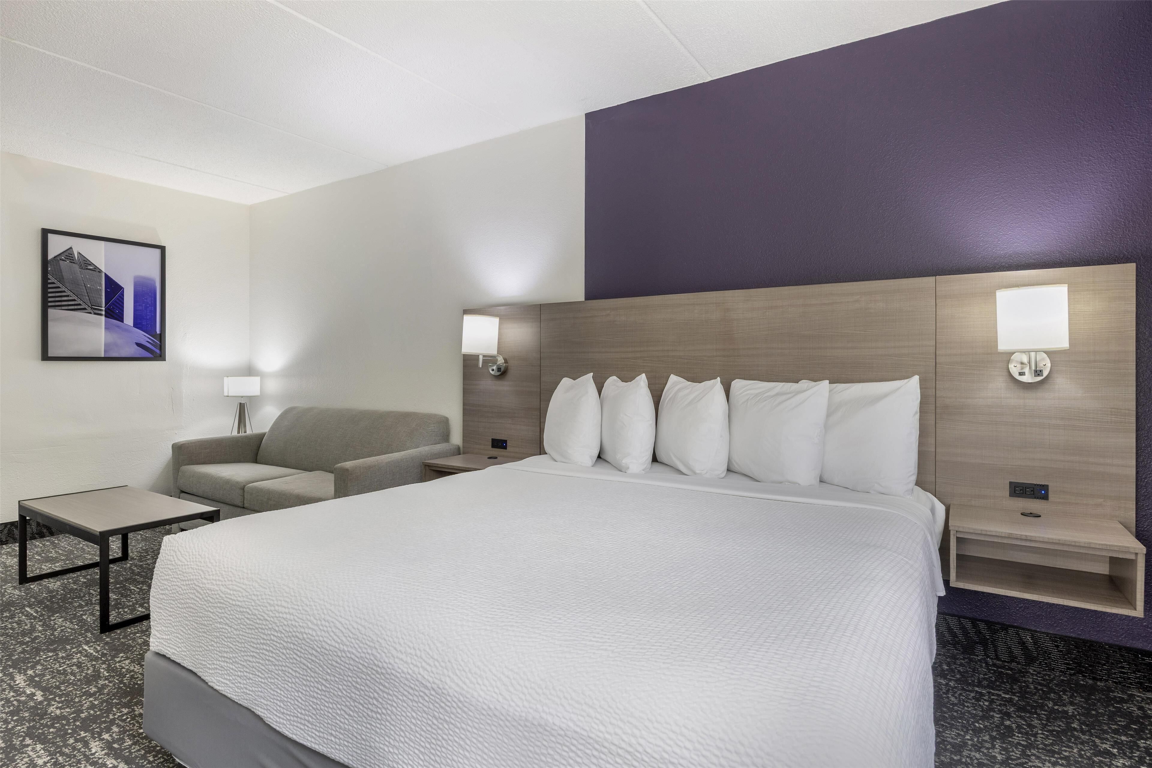 Una habitació d'hotel amb un llit gran, un sofà, una taula petita i dues taules de nit amb làmpades.