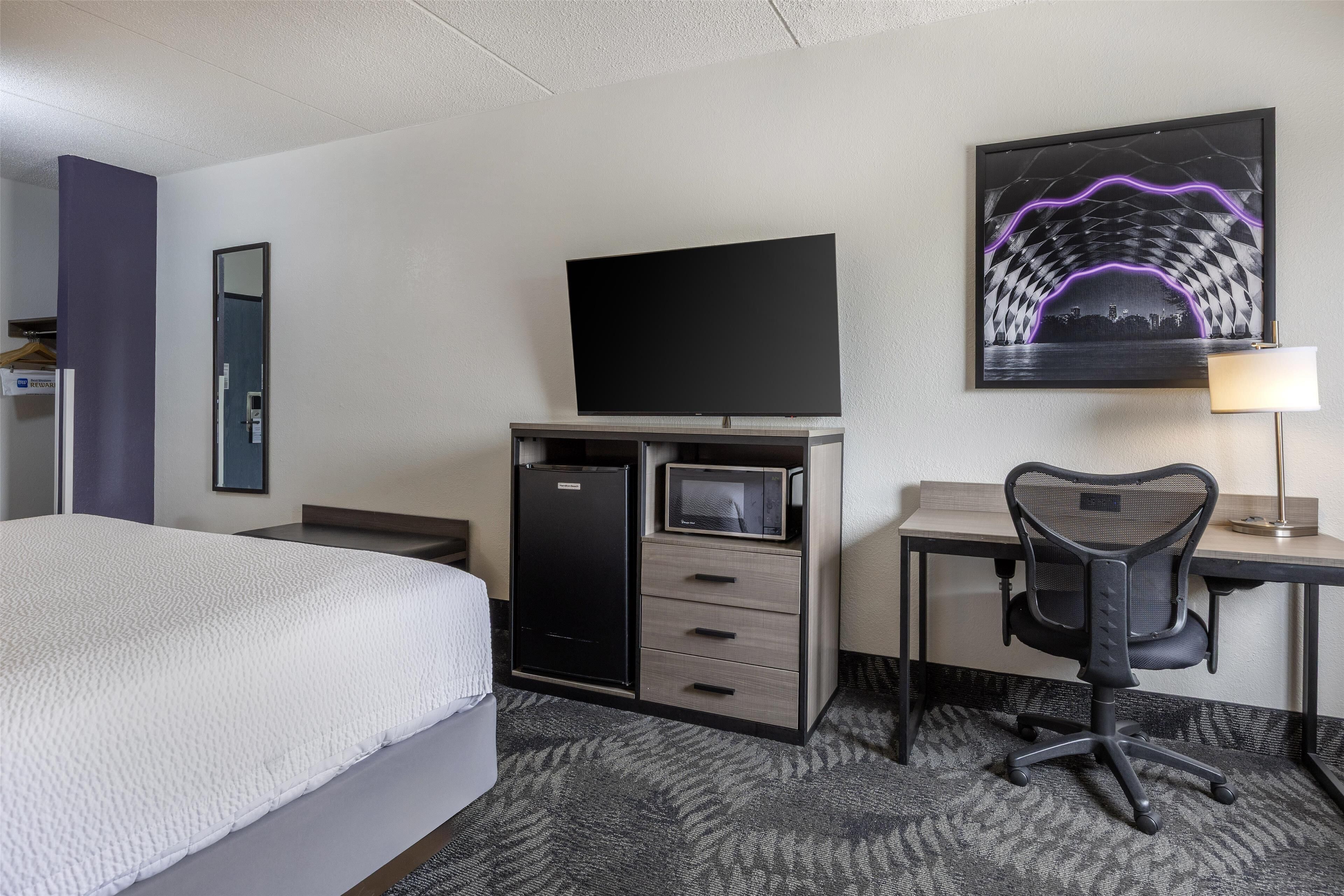 Ein Hotelzimmer mit einem Bett, einem Schreibtisch mit Computer, einem Fernseher und einer Mikrowelle.