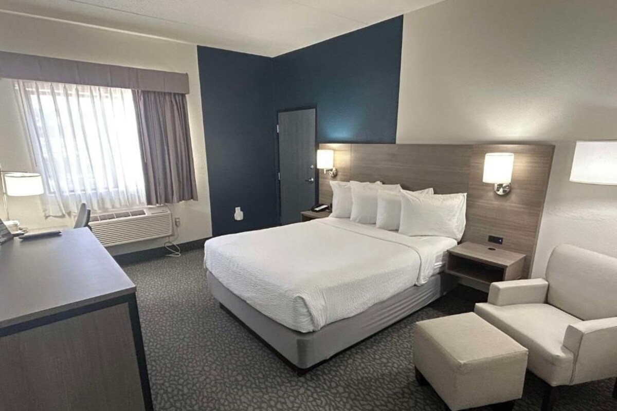 A hotel room with a large bed, bedside tables, a desk, a chair, and a window with curtains.