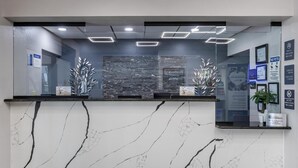 A reception desk with a marble design, a stone wall background, and a modern light fixture. - Best Western Bolingbrook Hotel (Bolingbrook)