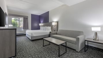 A hotel room with a bed, a sofa, a desk, and a small table.