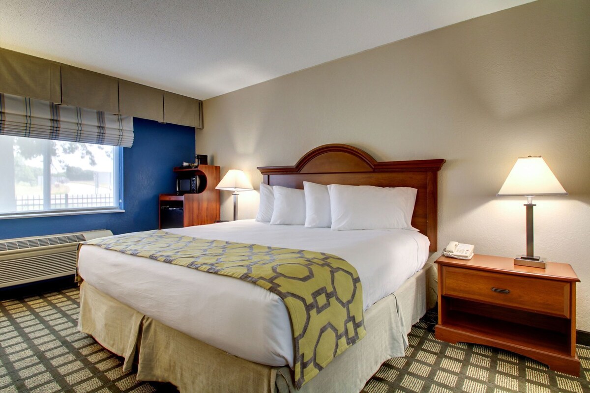 A hotel room with a bed, bedside lamps, a desk, and a window.