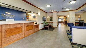 A reception area with a Baymont Inn & Suites sign, a reception desk, a seating area with chairs, and a hallway leading to other rooms.