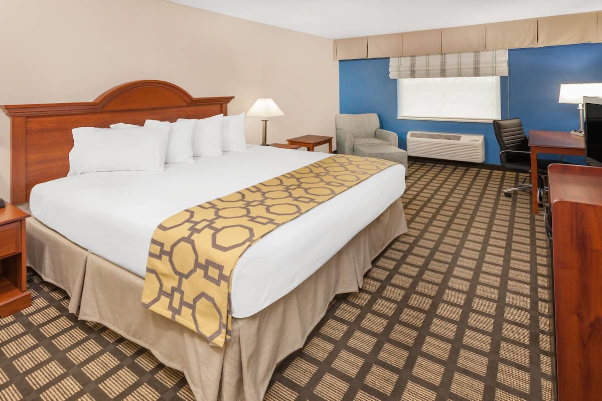 Une chambre d’hôtel avec un grand lit, un bureau, une chaise, une fenêtre avec des stores et un appareil de climatisation.