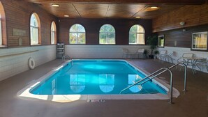 An indoor swimming pool with a wooden ceiling, arched windows, and a lifeguard sign.
