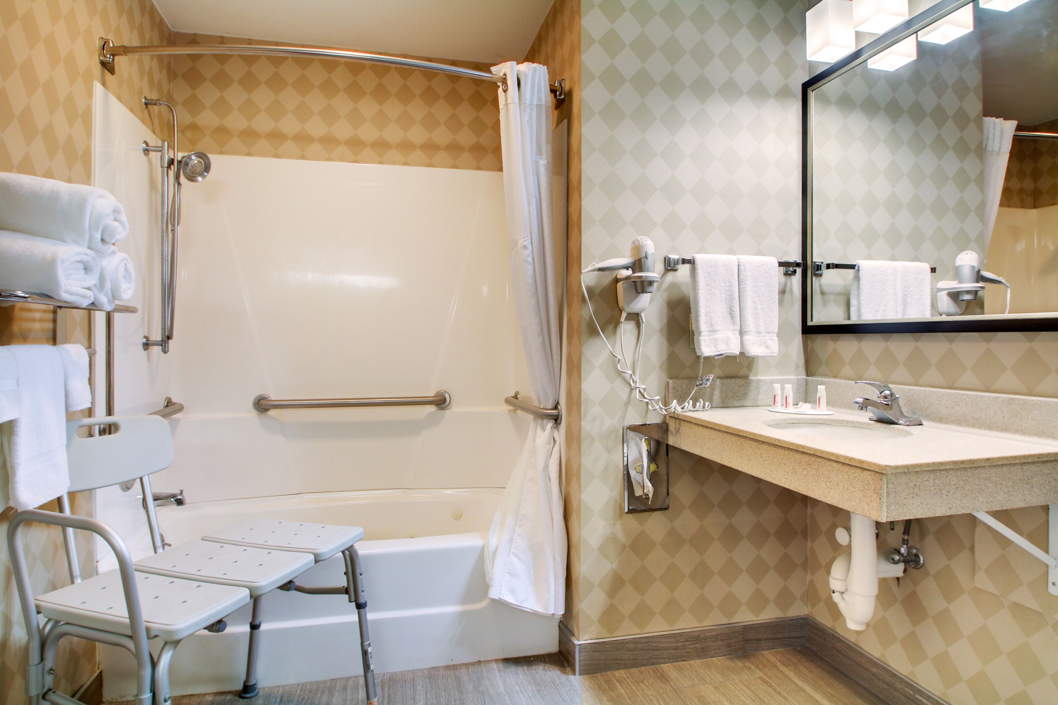 A bathroom with a shower, a sink, a mirror, and a wheelchair-accessible bench.