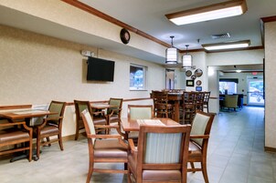 A dining area with wooden tables and chairs, a flat-screen TV mounted on the wall, and a clock.