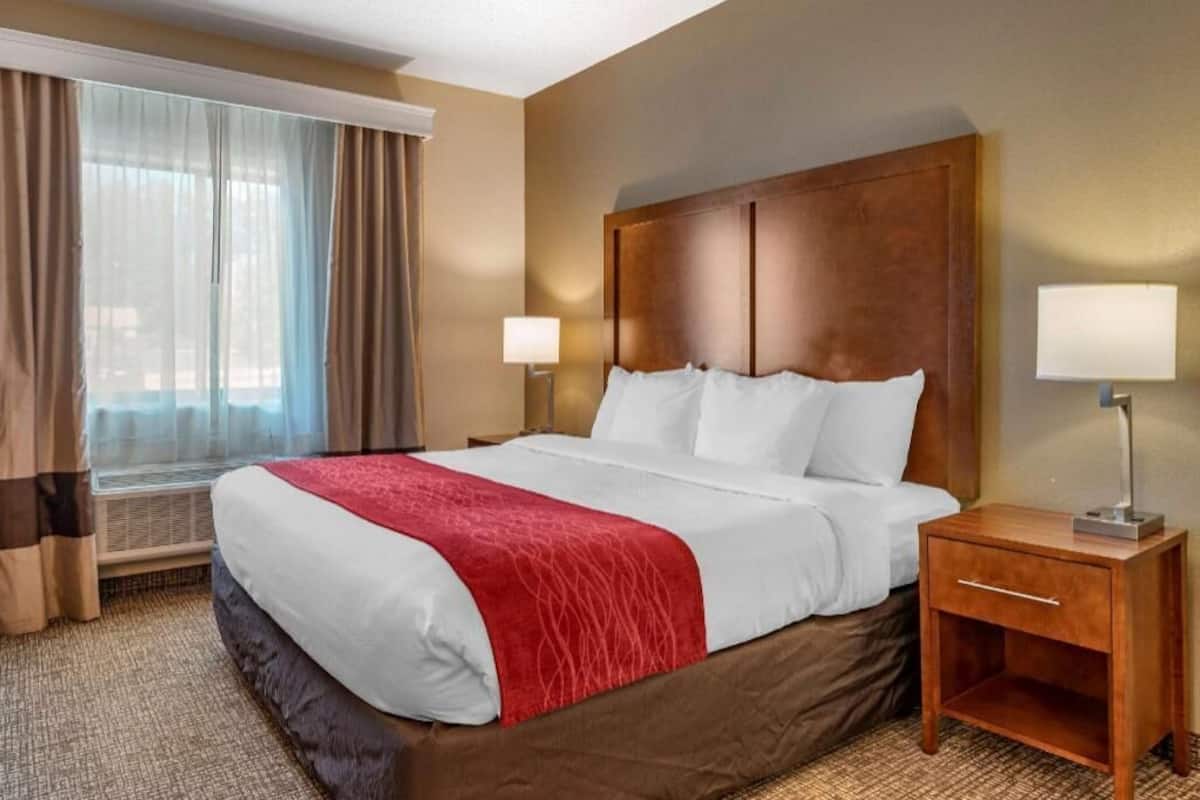 Ein Hotelzimmer mit einem großen Bett, zwei Nachttischlampen, einem Fenster mit Vorhängen und einem Holznachttisch.