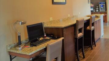 A kitchen area with a bar counter, bar stools, a computer setup, and a refrigerator.