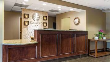 A reception desk with a stone accent wall, a clock, and a small table with potted plants.
