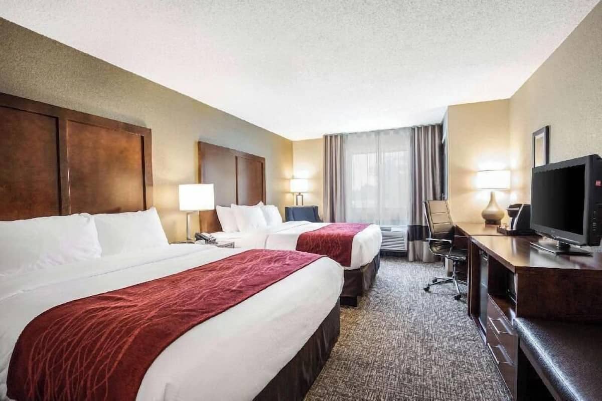 Ein Hotelzimmer mit zwei Betten, einem Schreibtisch mit Fernseher und einem Sessel.