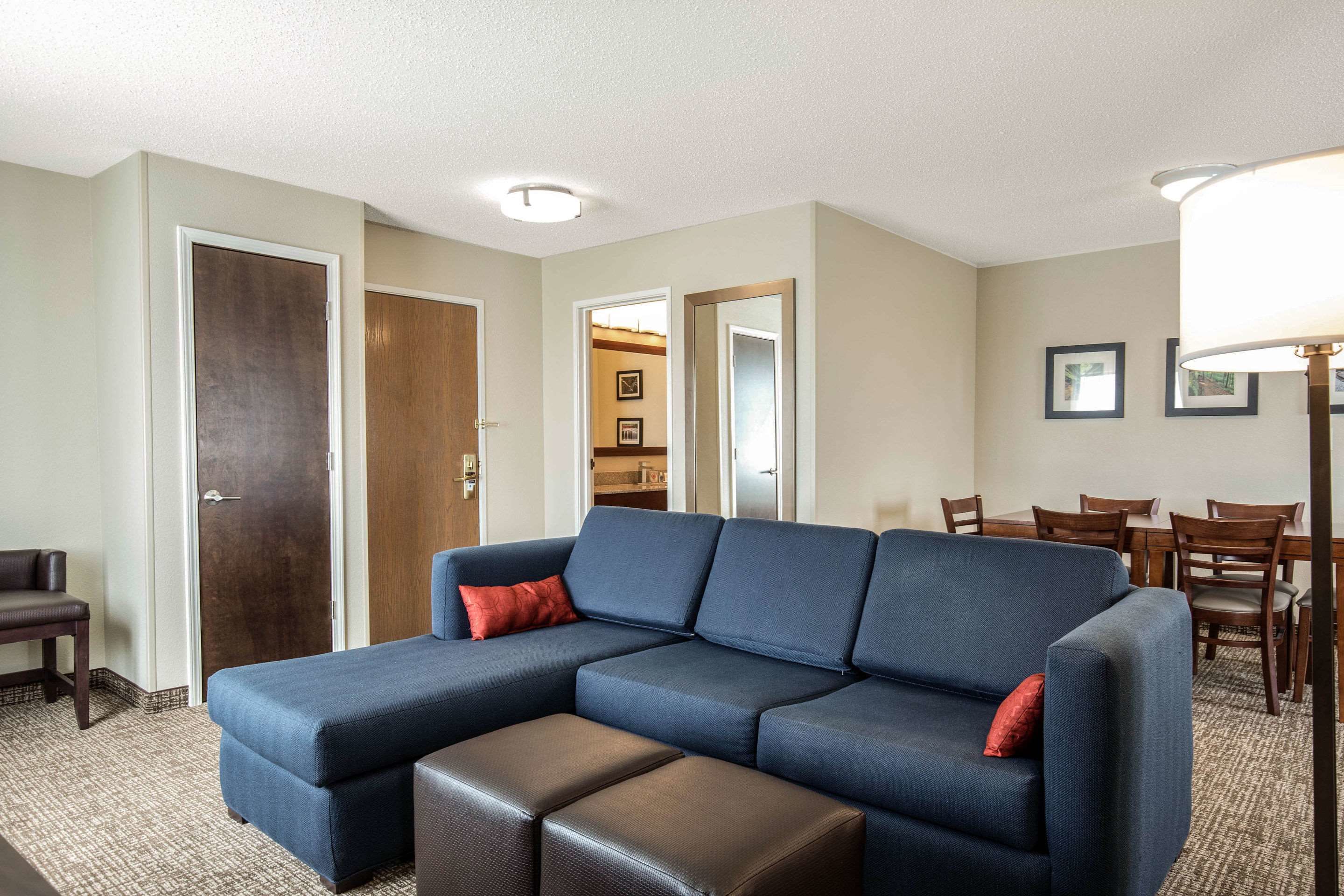 A living room with a sectional sofa, ottoman, dining table, chairs, and a lamp.