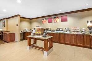 A hotel breakfast area with a buffet setup, including various food stations and a coffee bar.