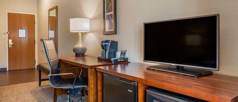 Une chambre d’hôtel équipée d’un bureau en bois, d’une télévision, d’un réfrigérateur et d’une chaise.