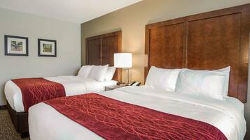 A hotel room with two beds, a wooden headboard, a lamp, and two framed pictures on the wall.