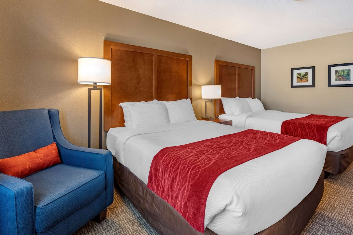 Ein Hotelzimmer mit zwei Betten, einem blauen Sessel und einem Holzkopfende.