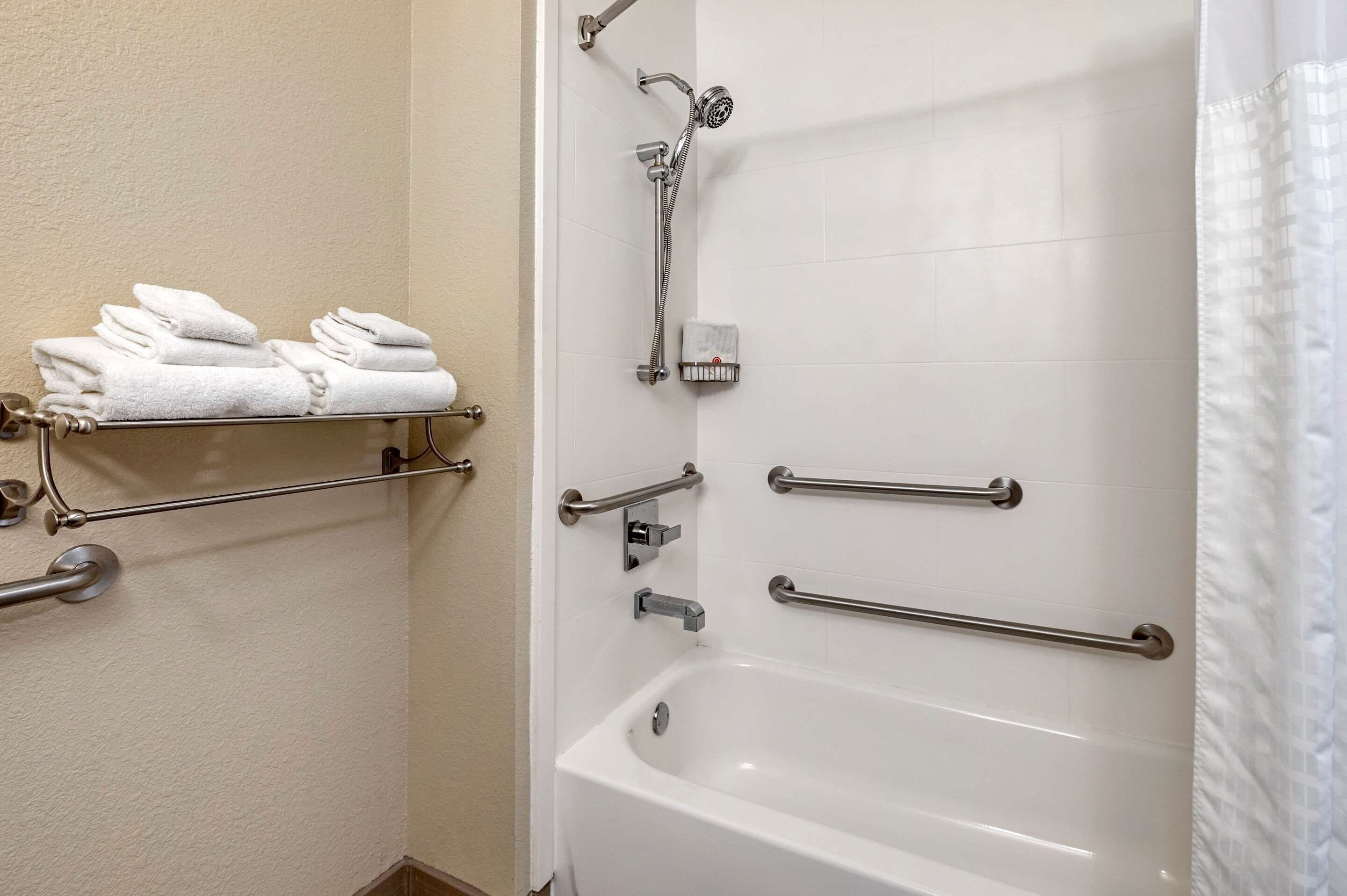 Un baño con bañera, barras de apoyo, toallero y ducha.