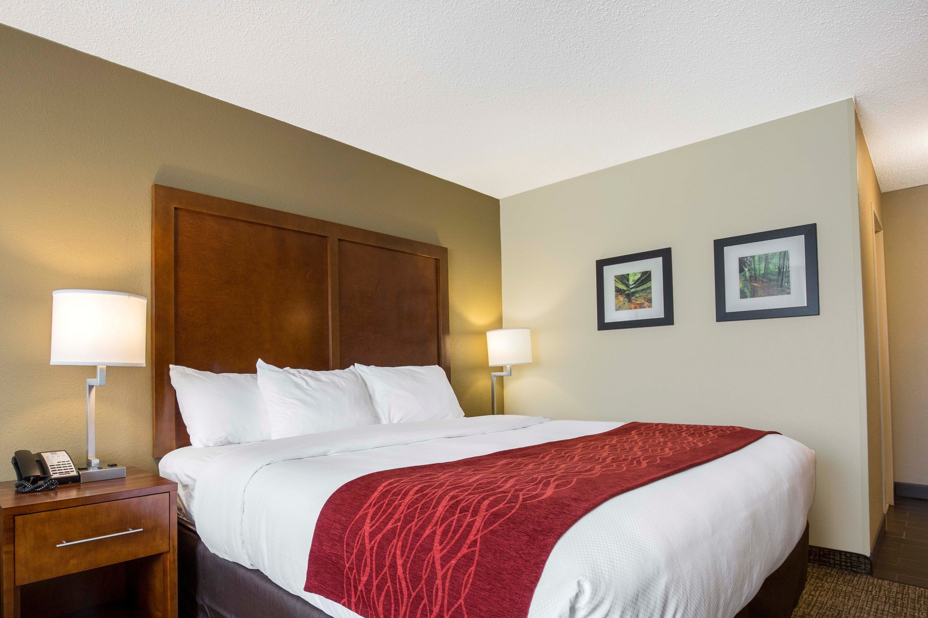 A hotel room with a large bed, two bedside lamps, a wooden headboard, and two framed pictures on the wall.