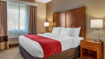 Habitación de hotel con una cama grande, dos lámparas de noche, una mesita de madera y una ventana con cortinas.
