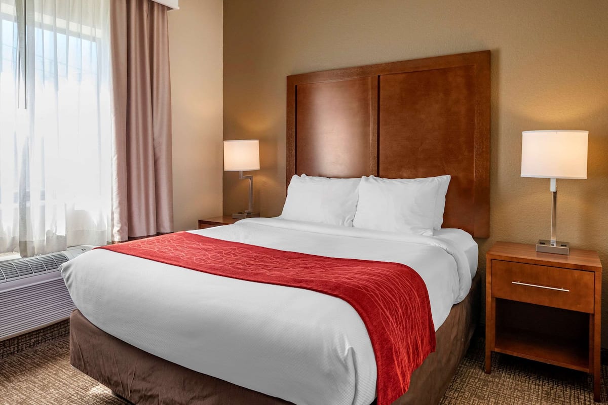 Ein Hotelzimmer mit einem großen Bett, zwei Nachttischen mit Lampen, einem Heizkörper und einem Fenster mit Vorhängen.