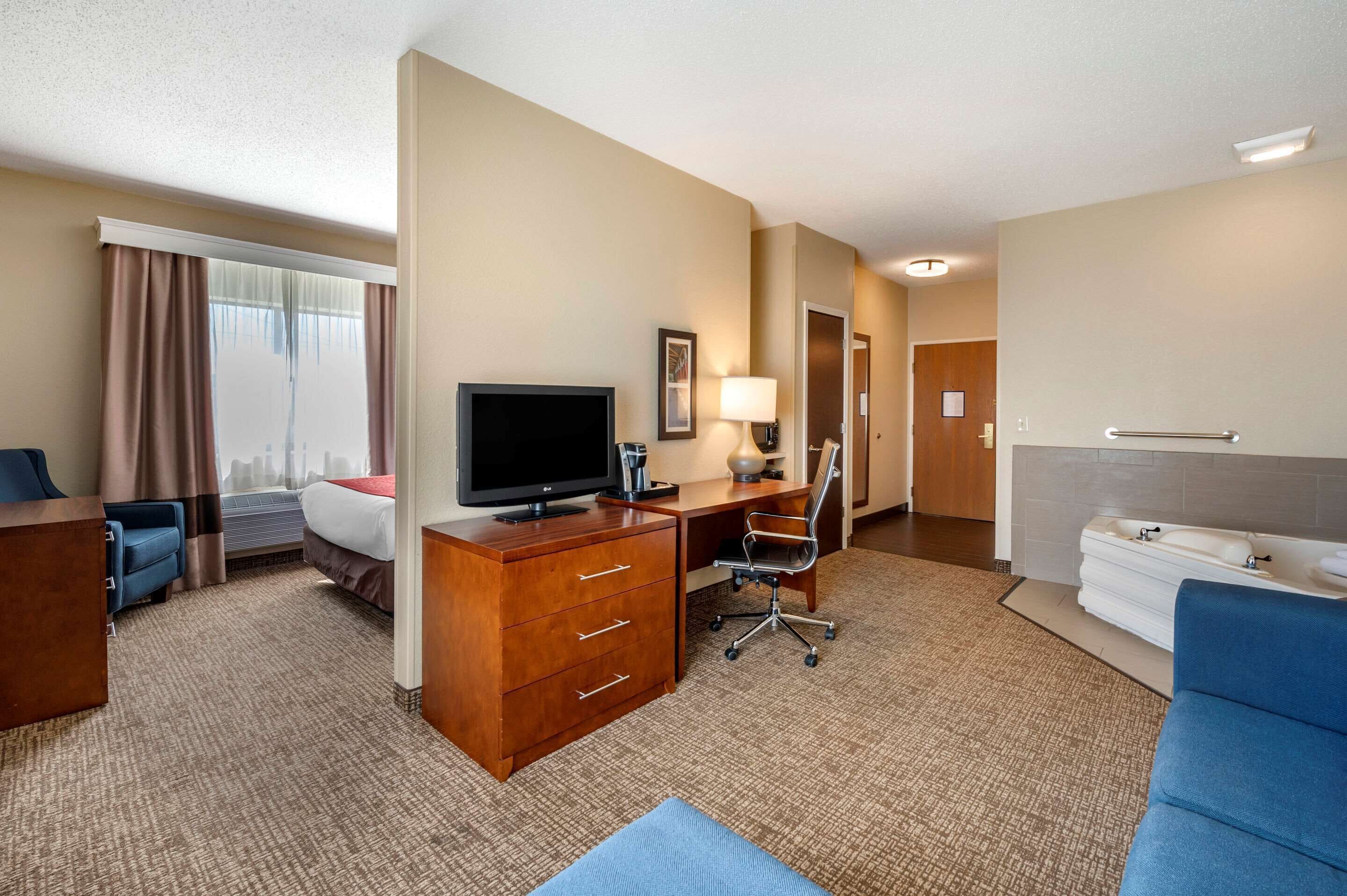 A hotel room with a bed, desk, television, lamp, and a bathroom with a sink and towel rack.