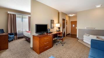A hotel room with a bed, desk, television, lamp, and a bathroom with a sink and towel rack.