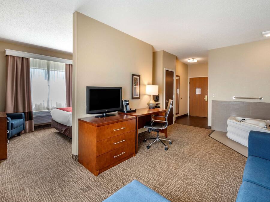 A hotel room with a bed, desk, television, lamp, and a bathroom with a sink and towel rack.