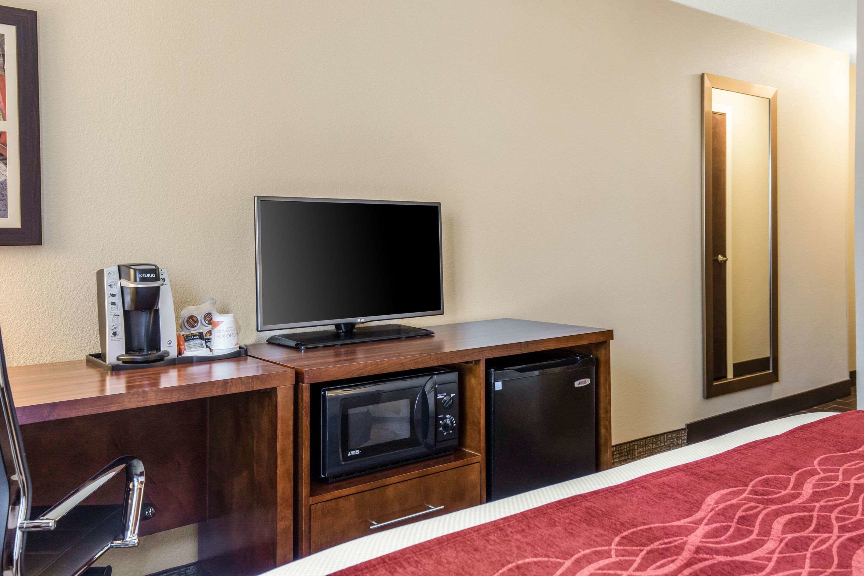 A hotel room with a bed, a TV, a coffee maker, a microwave, and a refrigerator.