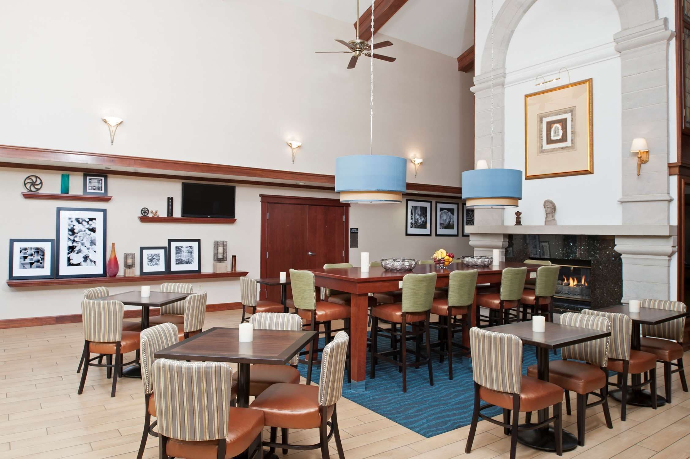 Ein Hotel-Speisesaal mit mehreren Tischen, Stühlen, einem Kamin und gerahmten Bildern an den Wänden.