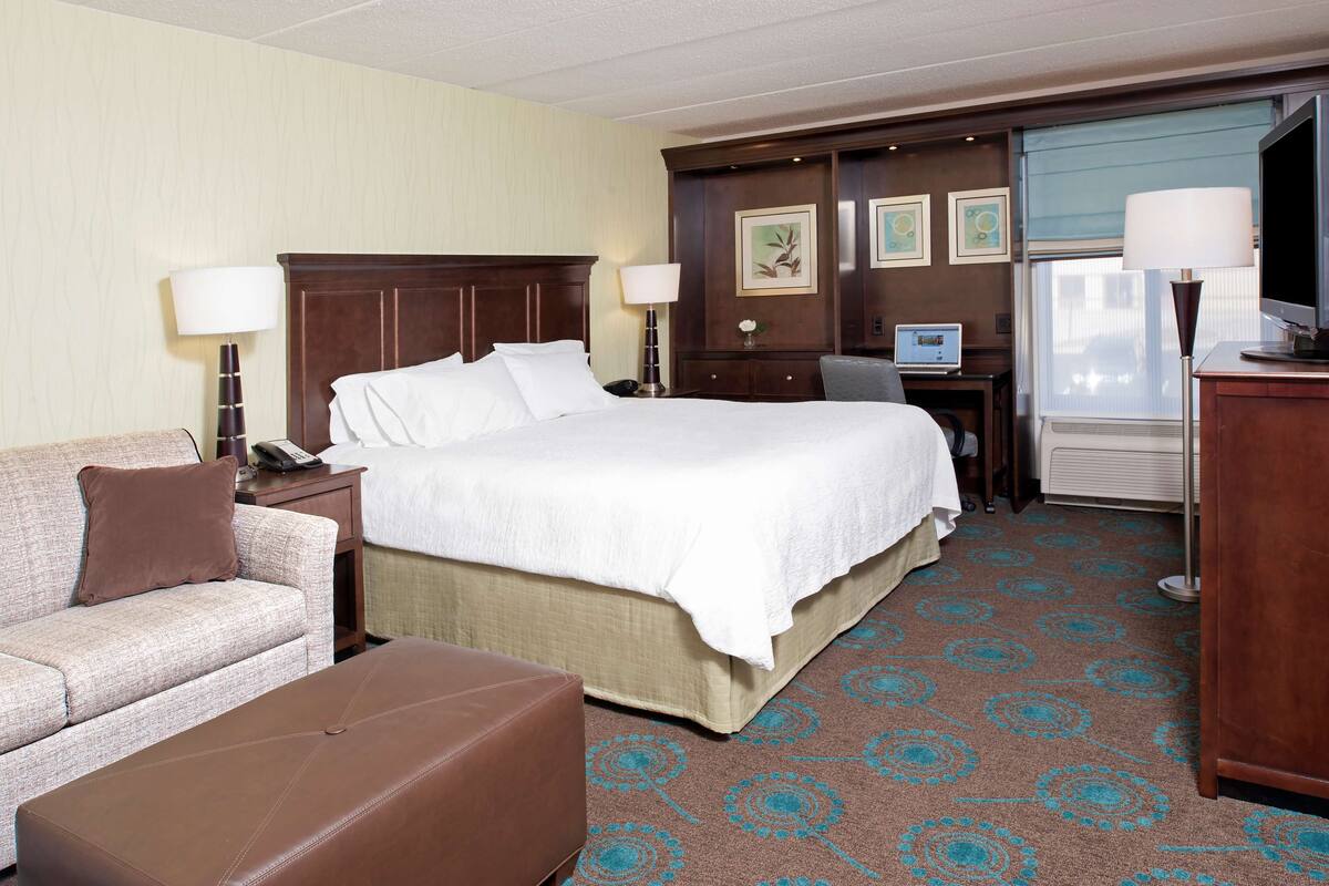 A hotel room with a large bed, a sofa, a desk with a computer, and a television.