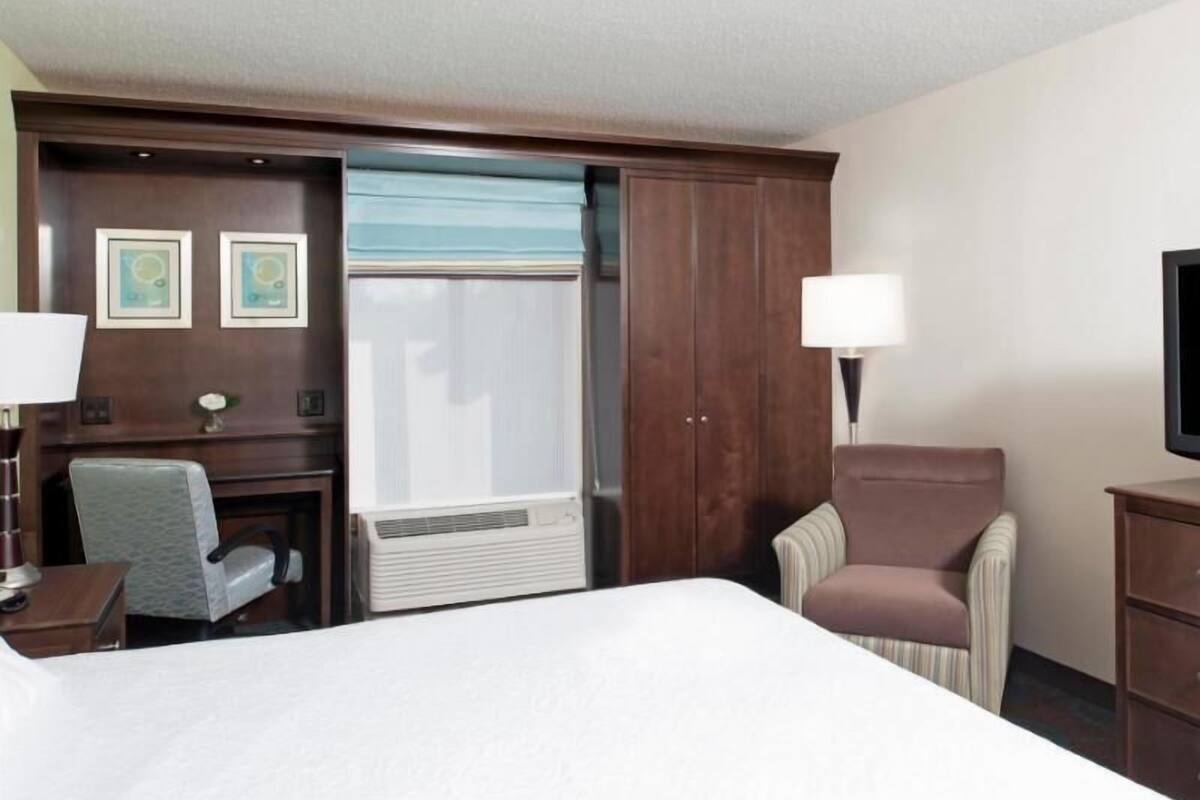 A hotel room with a bed, a desk, a chair, a wardrobe, a television, and a window with blinds.