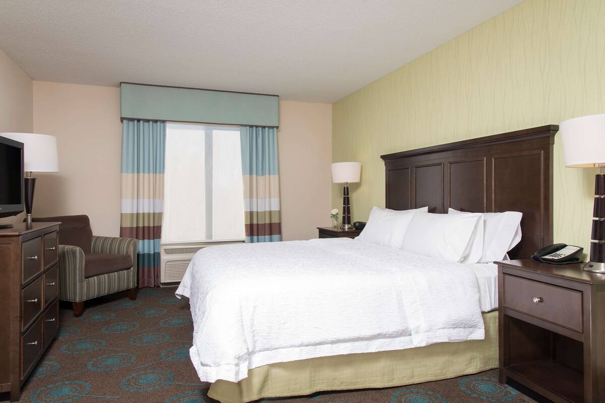 A hotel room with a bed, a chair, a dresser, a nightstand, and a television.