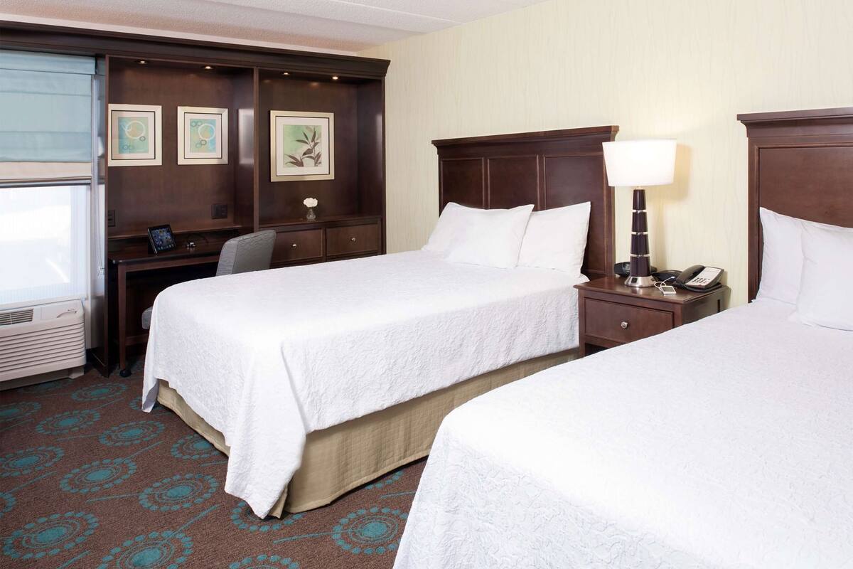A hotel room with two beds, a desk, a chair, a lamp, and a phone on the nightstand.