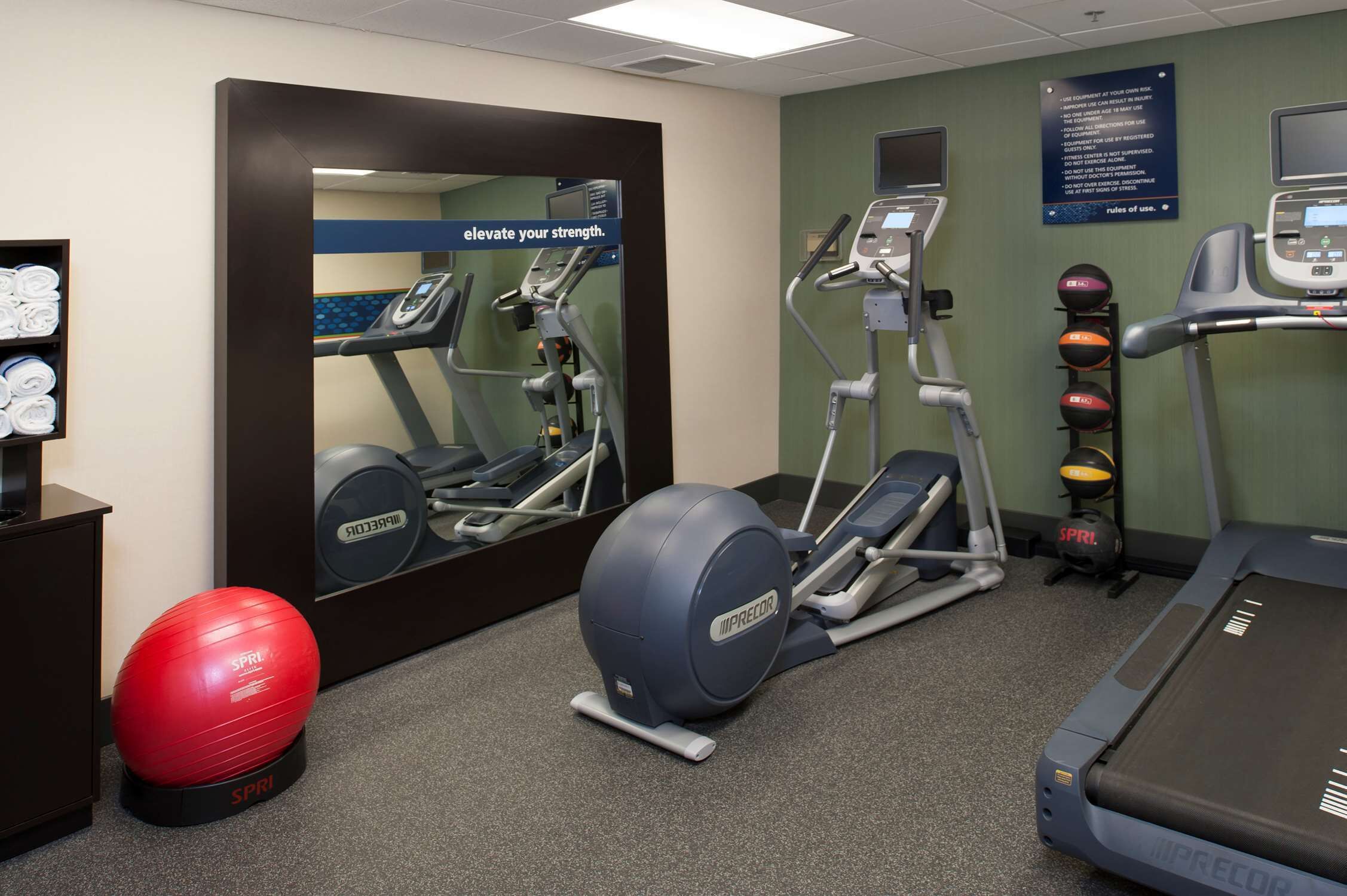 A fitness room with treadmills, an elliptical, and a red exercise ball.